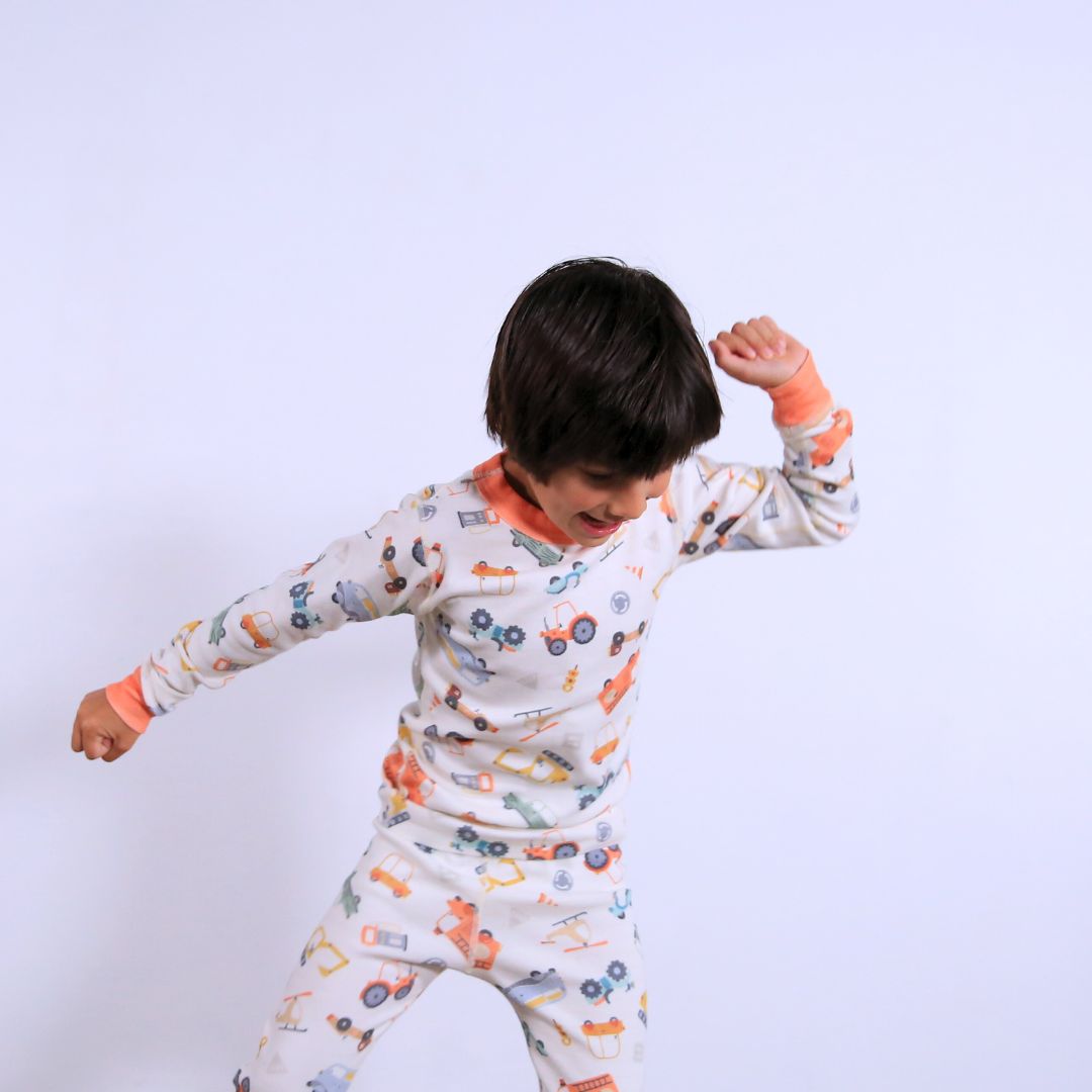Child against white wall wearing Organic pajamas made in San Francisco with vintage cars and trucks prints. Detail of flatlog seam for sensitive skin. 100% cotton threads to avoid irritation.