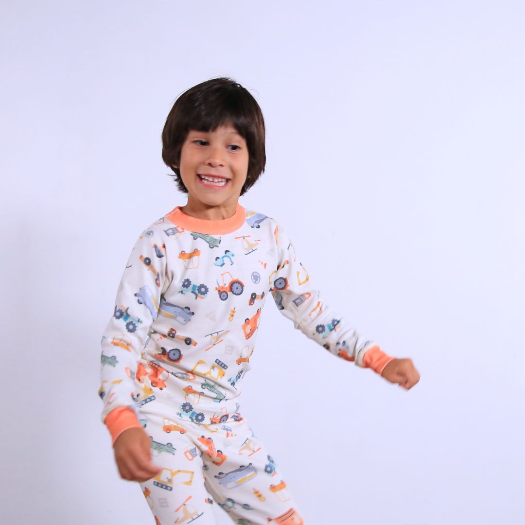 Child against white wall wearing Organic pajamas made in San Francisco with vintage cars and trucks prints. Detail of flatlog seam for sensitive skin. 100% cotton threads to avoid irritation.