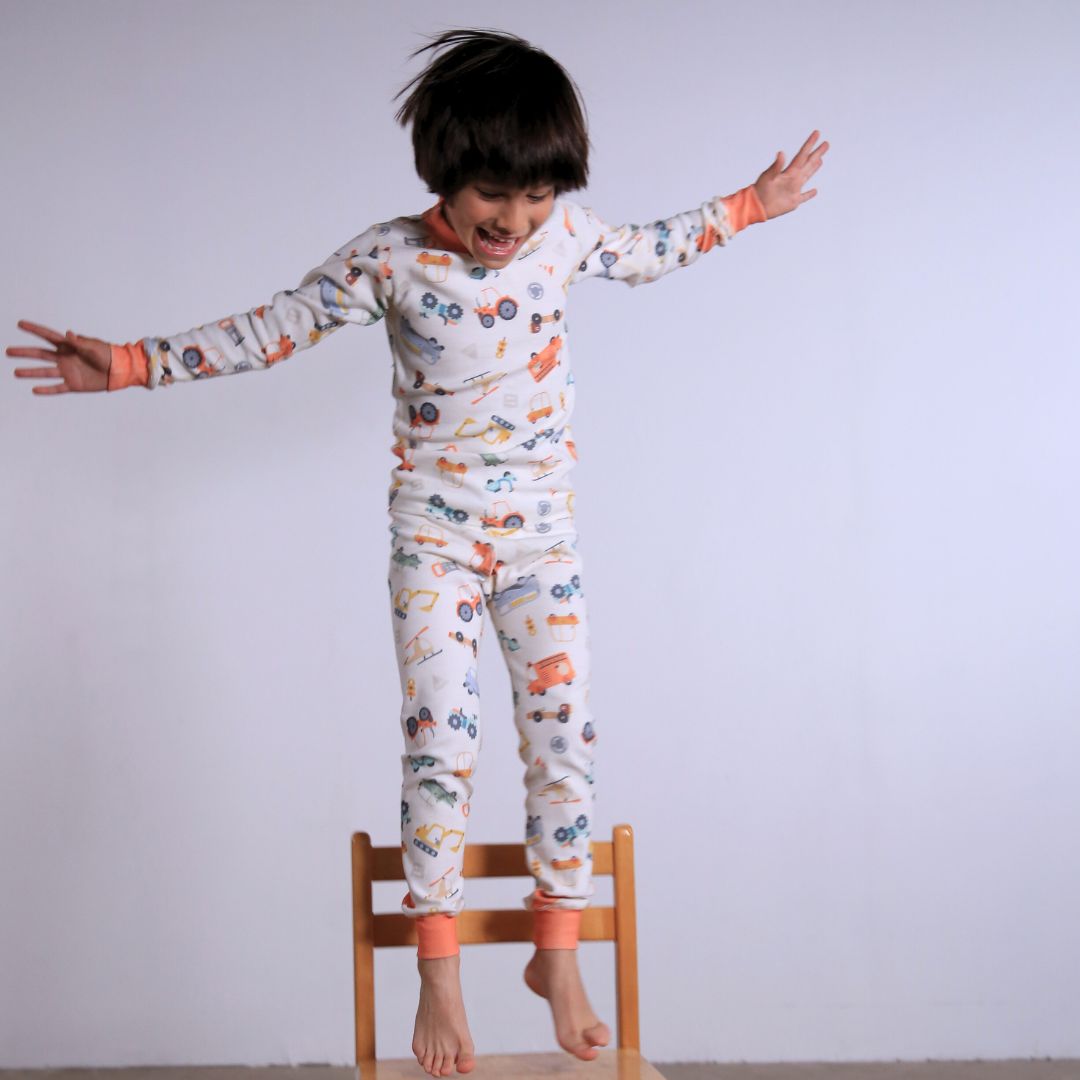 Child against white wall wearing Organic pajamas made in San Francisco with vintage cars and trucks prints. Detail of flatlog seam for sensitive skin. 100% cotton threads to avoid irritation.