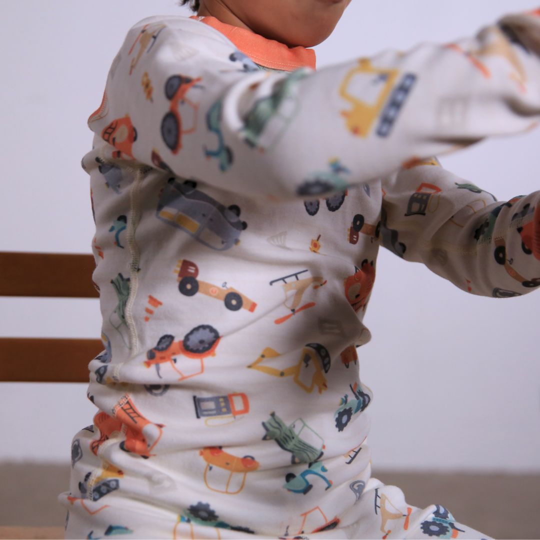 Child against white wall wearing Organic pajamas made in San Francisco with vintage cars and trucks prints. Detail of flatlog seam for sensitive skin. 100% cotton threads to avoid irritation.