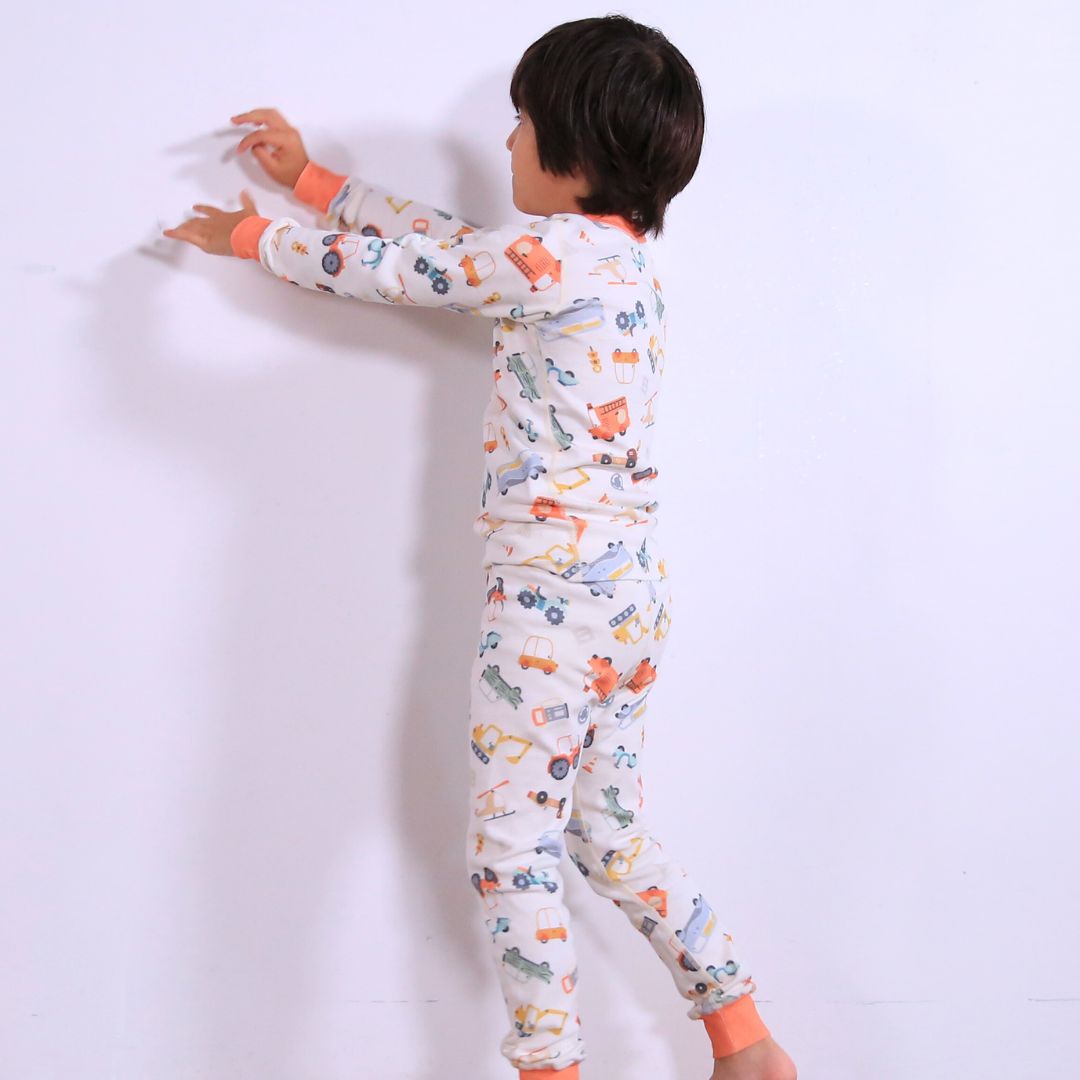 Child against white wall wearing Organic pajamas made in San Francisco with vintage cars and trucks prints. Detail of flatlog seam for sensitive skin. 100% cotton threads to avoid irritation.