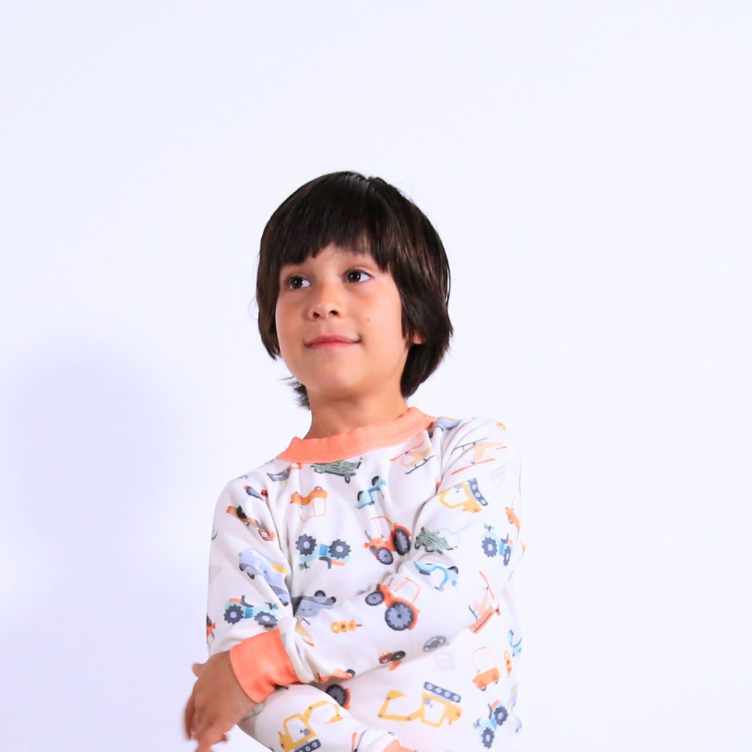 Child against white wall wearing Organic pajamas made in San Francisco with vintage cars and trucks prints. Detail of flatlog seam for sensitive skin. 100% cotton threads to avoid irritation.