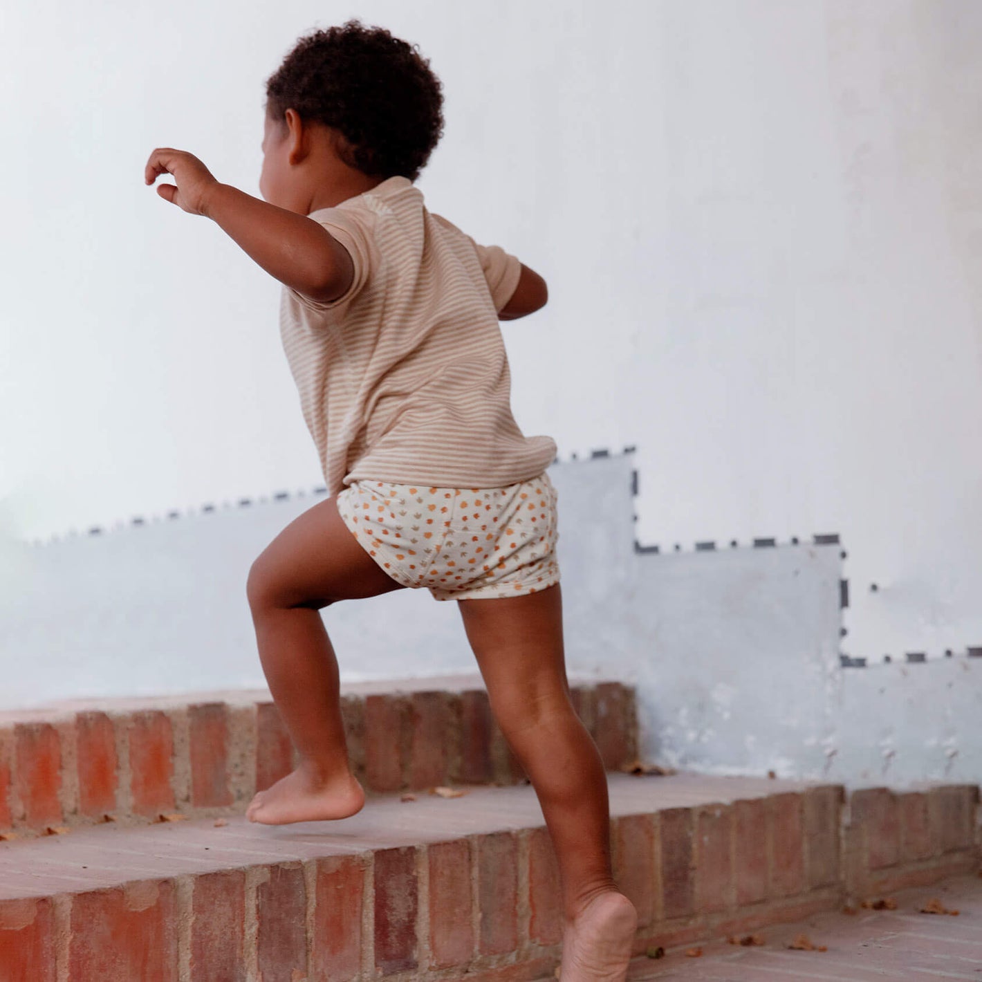 A child running up the stairs wearing Mukupati's potty training pants with dino's footprints artwork.